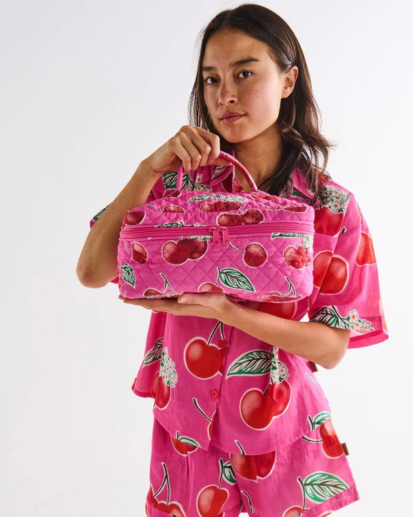 Person wearing a pink outfit with cherry pattern holding a matching pink bag. Kip & Co. Toiletry bag.